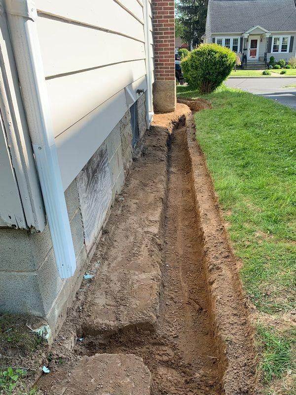 Drainage trench excavated along a home's foundation, ready for pipe and stone